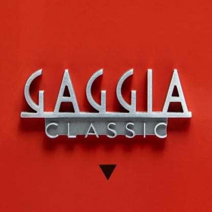 A metallic silver 3D lettering sign reading 'GAGGLIA CLASSIC' on a solid red background, with a small black inverted triangle below.

