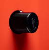 A glossy black cylindrical wall-mounted hook with a stylized silver emblem on the front, set against a solid bright red background.

